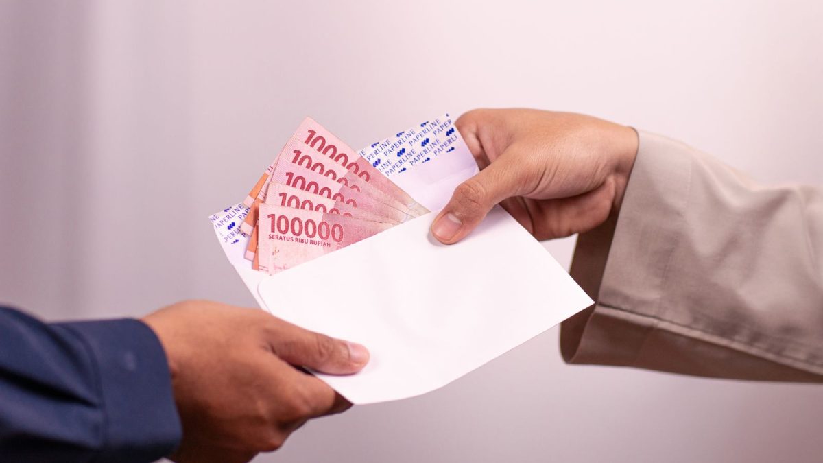 Dua tangan memberikan amplop putih berisi uang rupiah pecahan seratus ribu