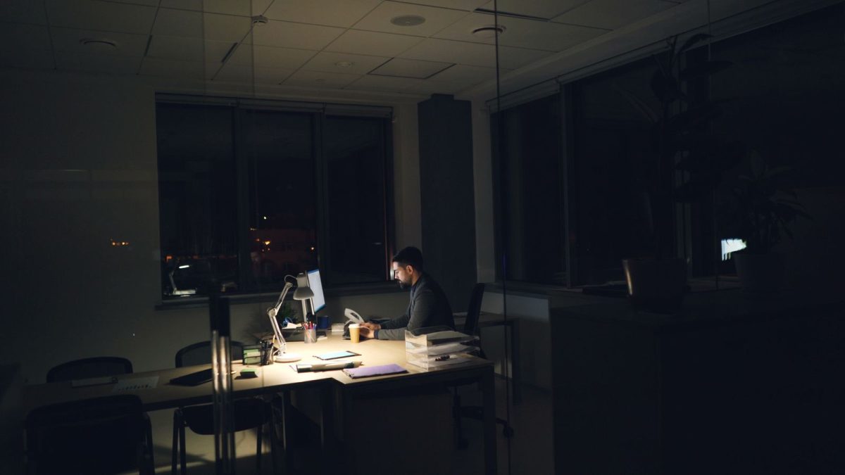 Karyawan pria bekerja sendirian di meja kantor yang gelap pada malam hari