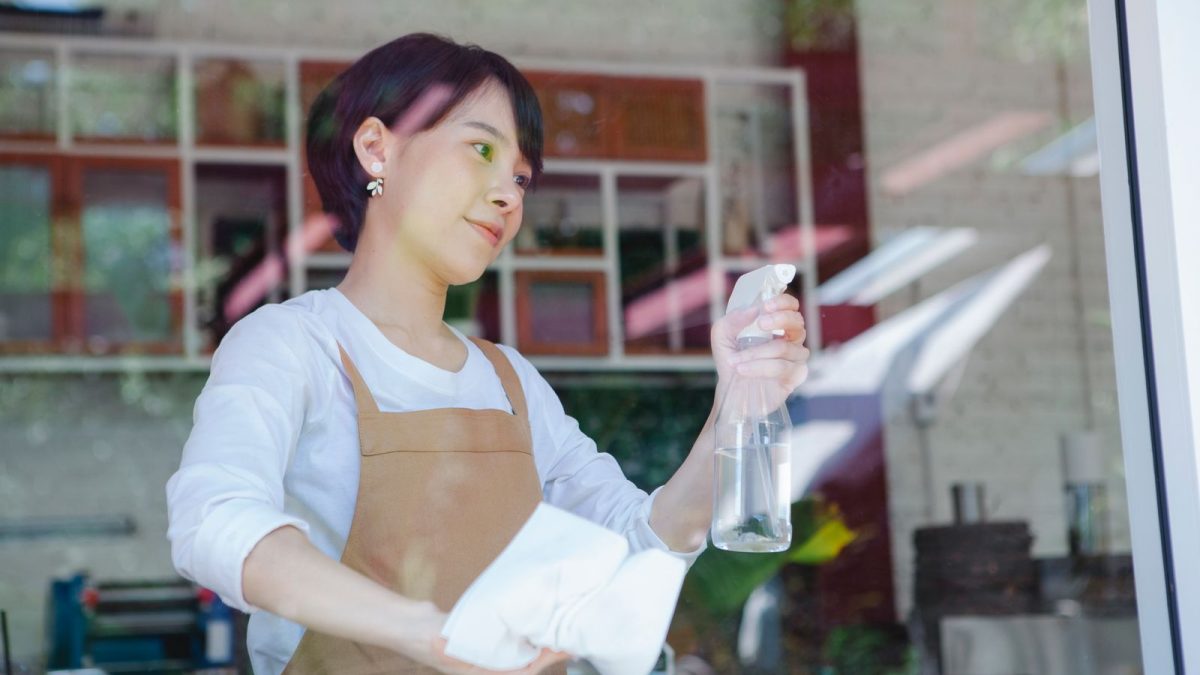 Karyawati berapron membersihkan kaca depan toko sebagai bagian dari rutinitas kerja