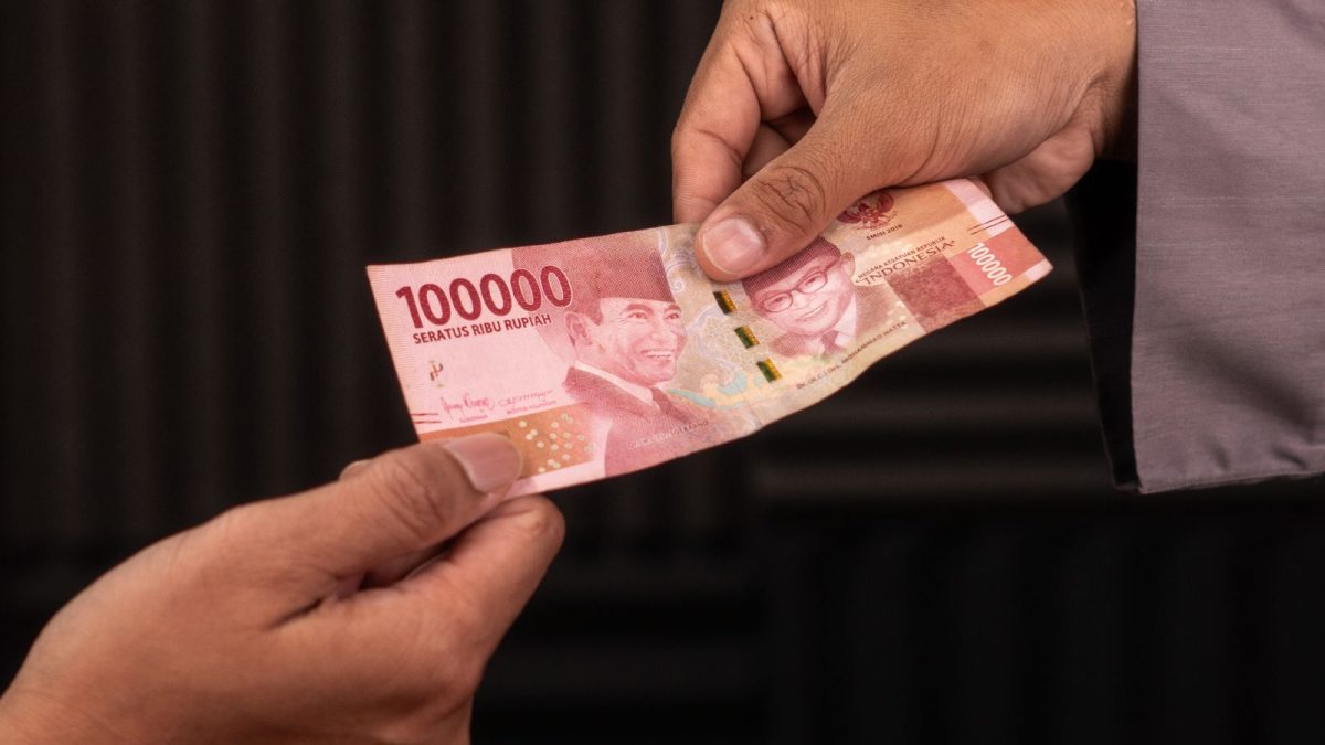 Tangan menyerahkan selembar uang rupiah seratus ribu kepada orang lain